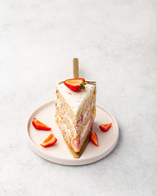 A slice of strawberry sponge cake with fresh berries and basil on a white background