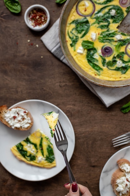 Slice of tasty omelet with vegetables on a fork in a woman's hand. Wood . Top view.