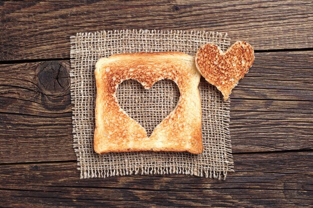 Slice of toast bread with cut out heart shape on vintage wooden background