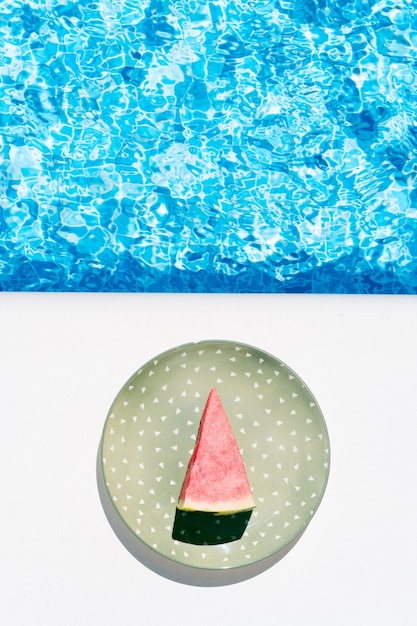 A slice of watermelon on a green plate by the pool concept of summer holidays and food