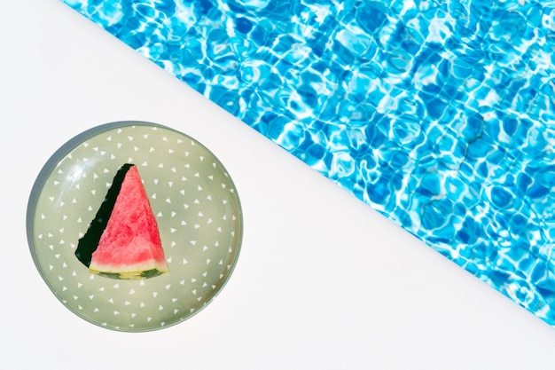 A slice of watermelon on a green plate by the pool concept of summer holidays and food