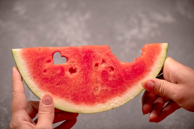 A slice of watermelon in hands with a heart-shaped hole