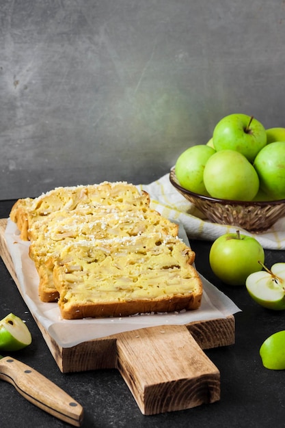 Sliced apple and coconut oaf cake on wooden cutting board on dark background