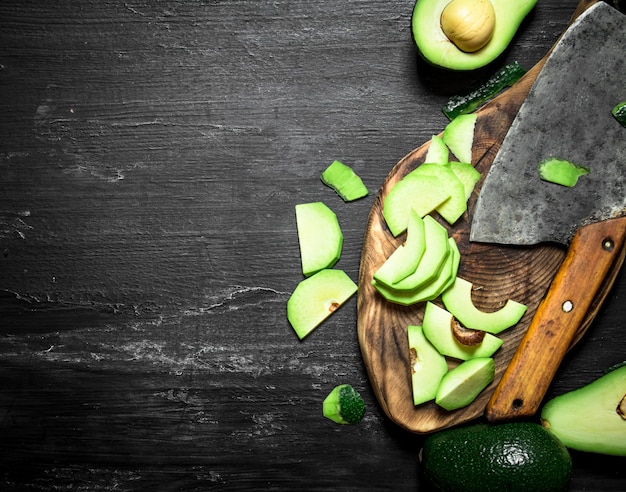 Sliced avocado with a hatchet on the Board. On a black wooden background. Top view.