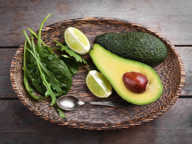 Sliced avocado with lime spinach and arugula on wooden plate