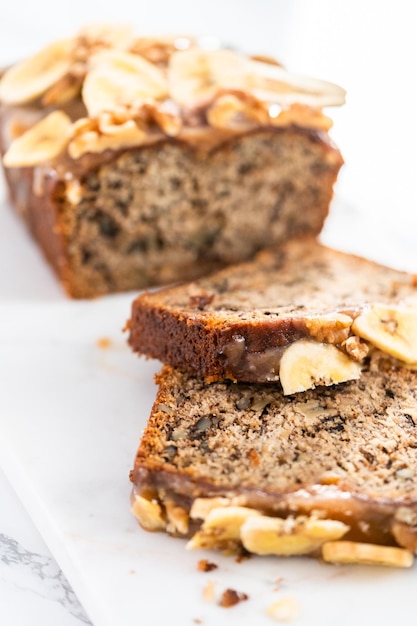 Sliced banana nut bread drizzled homemade caramel on a marble cutting board.