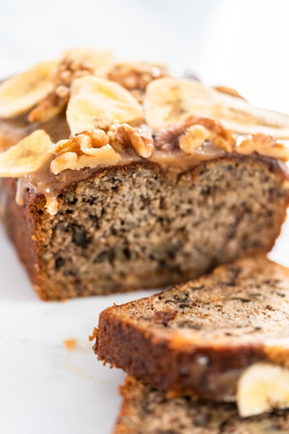 Sliced banana nut bread drizzled homemade caramel on a marble cutting board.