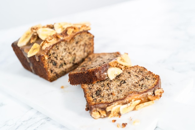 Sliced banana nut bread drizzled homemade caramel on a marble cutting board.