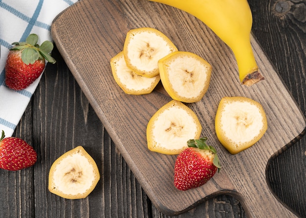 Sliced bananas with strawberries on a wooden desk close up