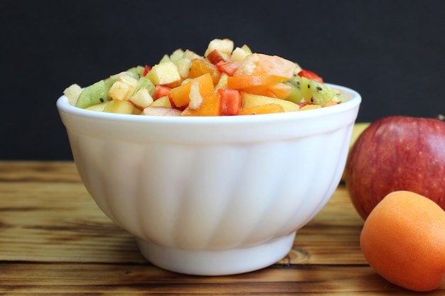 Sliced berries and fruits are on a plate for making a diet salad. Low-calorie bright breakfast for weight loss on a wooden table.