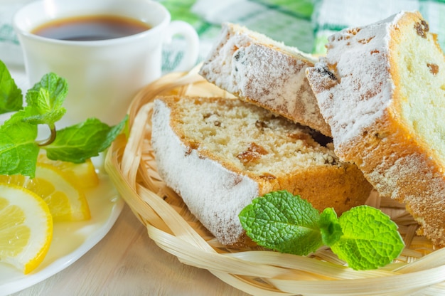 Sliced biscuit cake, a cup of tea, lemon slices and mint leaves