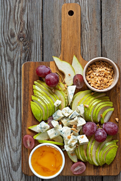 Sliced Blue cheese, dor blue or roquefort and fruits (grapes, pears), nuts and honey on a board.