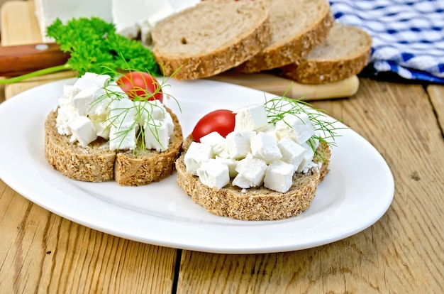 Sliced bread with cheese, tomato and dill on a plate, napkin, parsley, knife on background wooden boards