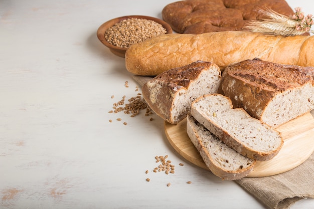 Sliced bread with different kinds of fresh baked bread on a white wooden surface. side view, copy space.