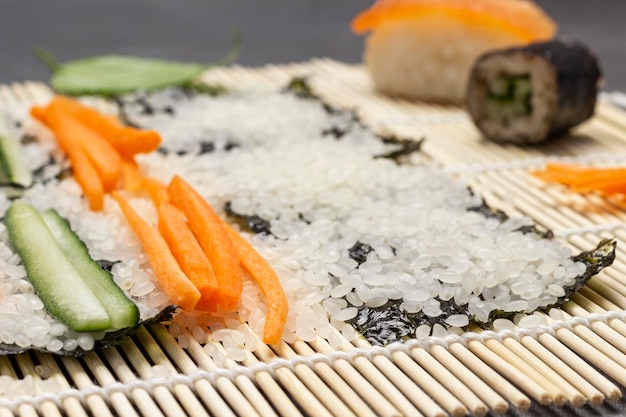 Sliced carrots cucumbers and rice on nori sheet on bamboo mat