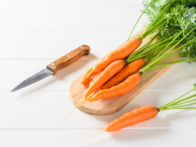 Sliced carrots with a knife on a cutting Board and a bunch of carrots on a white rustic table.