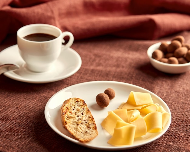 Sliced cheese toast and sweets lie on a white plate The plate is on a brown tablecloth Behind the