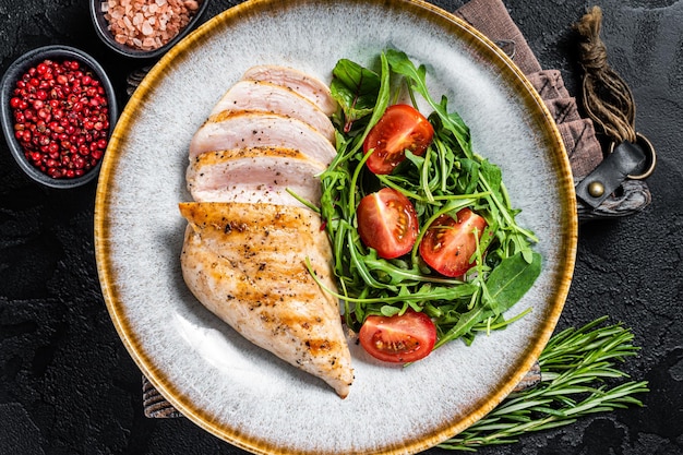 Sliced chicken breast fillet steak with green salad in a plate Black background Top view