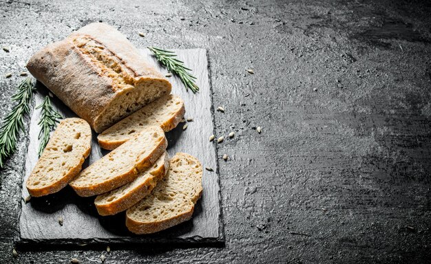 Photo sliced ciabatta bread on a stone board with rosemary