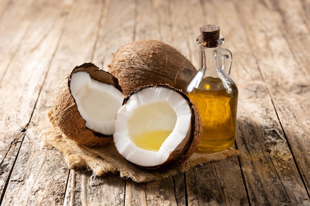 sliced coconuts with oil inside and bottle of coconut oil on wooden table