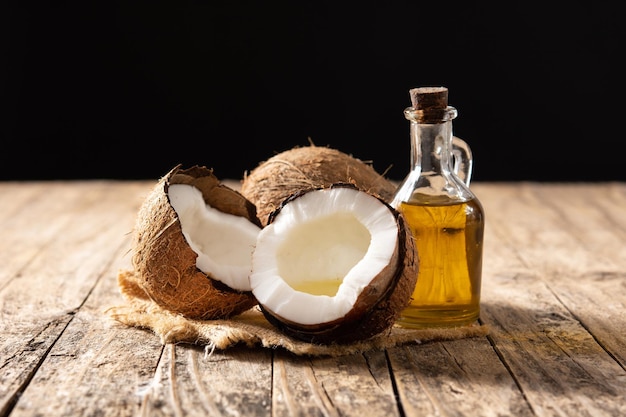 sliced coconuts with oil inside and bottle of coconut oil on wooden table