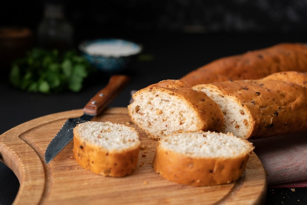 Sliced french baguette on a wooden board, bread knife laying around