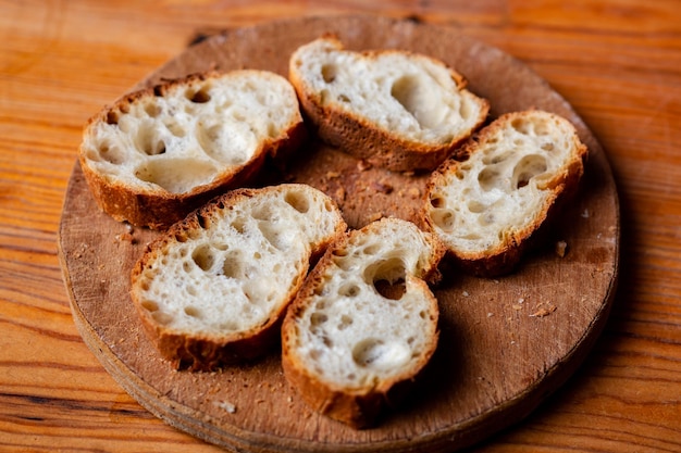 Sliced French baguette on a wooden board on a light background Bread with big holes Preparing for bruschetta