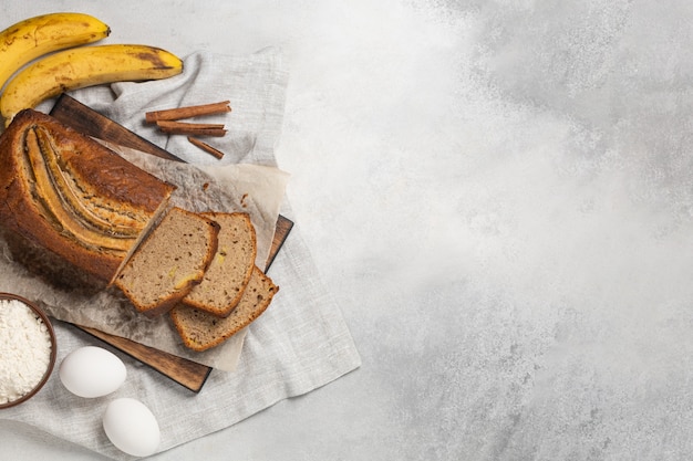 Sliced fresh banana bread with ingredients on light background