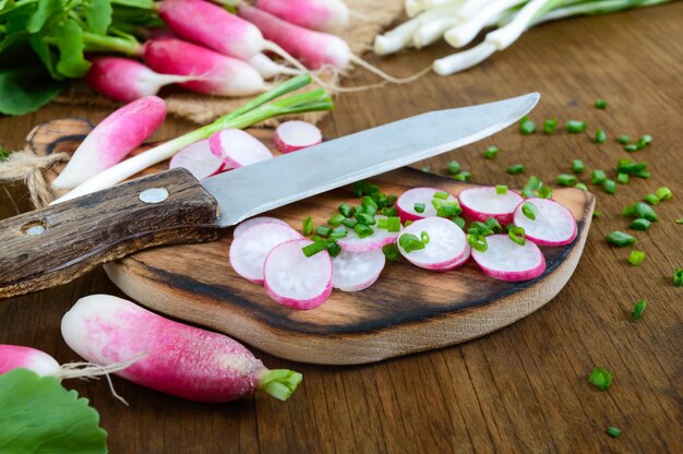 Sliced fresh red radishes and green young onions on white wooden background.  Healthy diet with radish. Ingredients for a light spring vegetable salad.