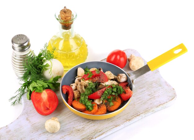 Sliced fresh vegetables in pan on wooden board isolated on white