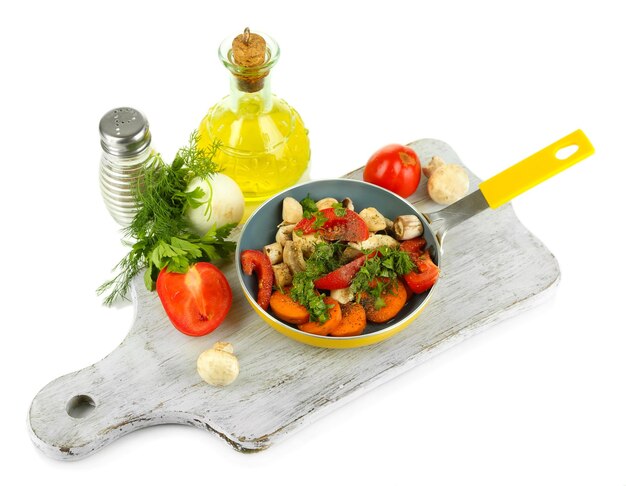 Sliced fresh vegetables in pan on wooden board isolated on white