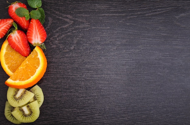 Sliced fruit (strawberries, kiwi, orange, banana) on a black background