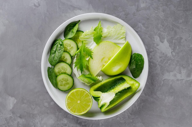 Sliced green fruits and vegetables on a gray background. Fresh green diet food in a white plate. Healthy vegetarian food concept. Copy space. Top view