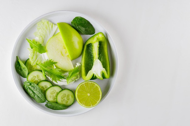 Sliced green fruits and vegetables in a white plate. Fresh green diet food on white background. Healthy vegetarian food concept. Copy space. Top view