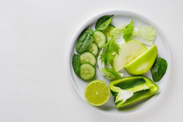 Sliced green fruits and vegetables in a white plate. Fresh green diet food on white background. Healthy vegetarian food concept. Copy space. Top view