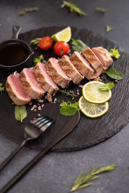 Sliced grilled cooked piece of tuna fillet on black stone serving board