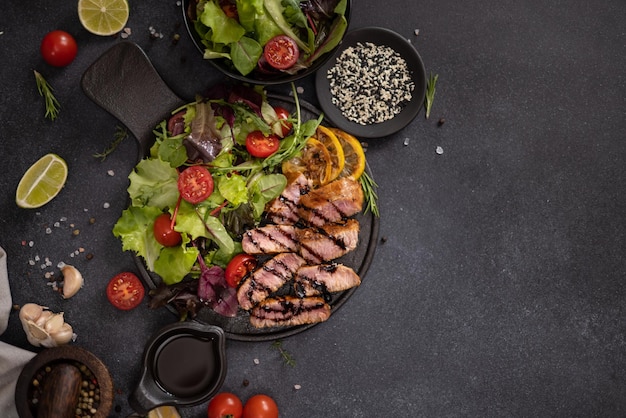 Sliced grilled organic tuna steak on black ceramic serving dish with salad on a table