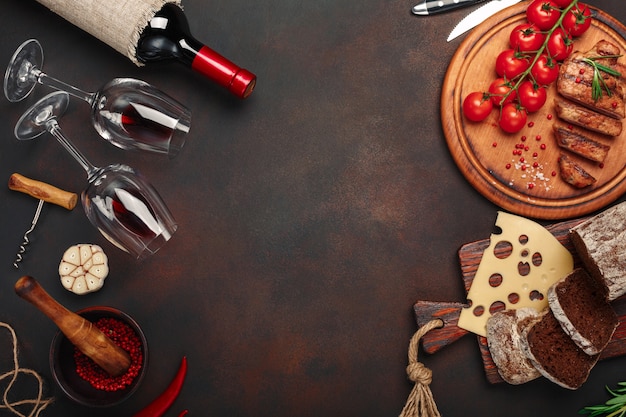 Sliced grilled pork steaks on a cutting board with cherry tomatoes, cheese, bread, garlic and rosemary