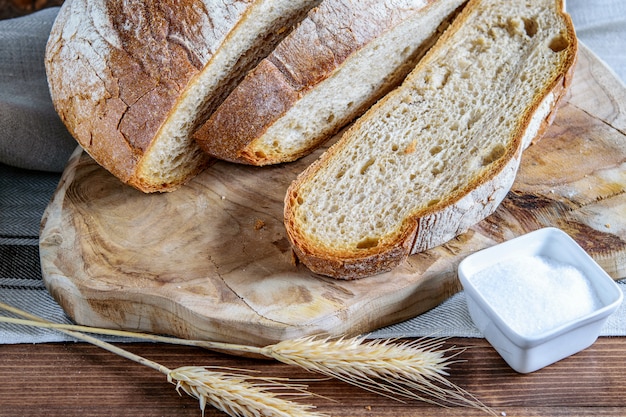 Sliced integral bread, wheat grains and salt on the wooden cutting board. Healthy homemade integral bread.