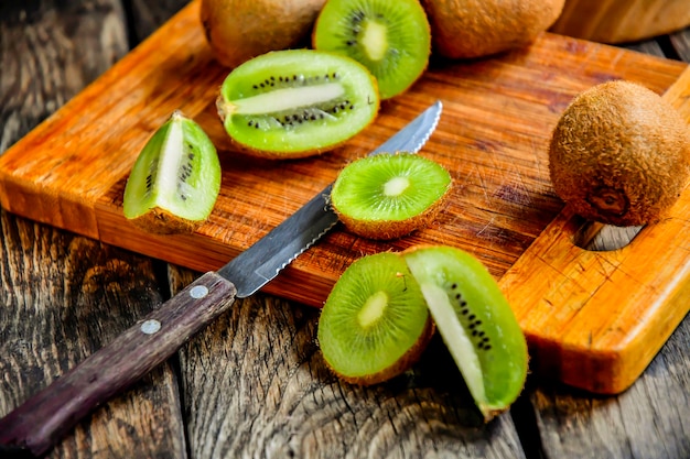 Sliced Kiwi on a kitchen board with a knife on a wooden table.