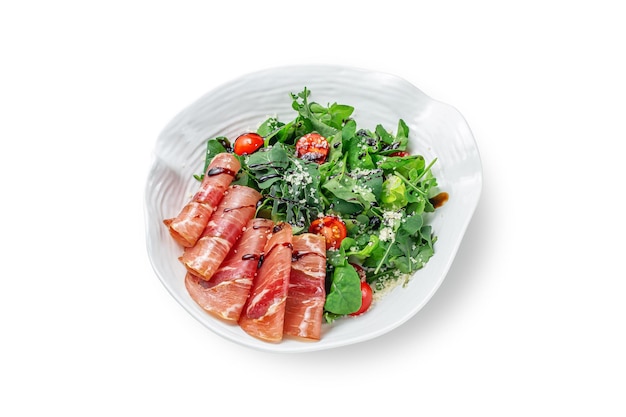 Sliced layers of beef, parma ham with cherry tomatoes on arugula leaves, seasoned with balsamic sauce in a plate on a white isolated background