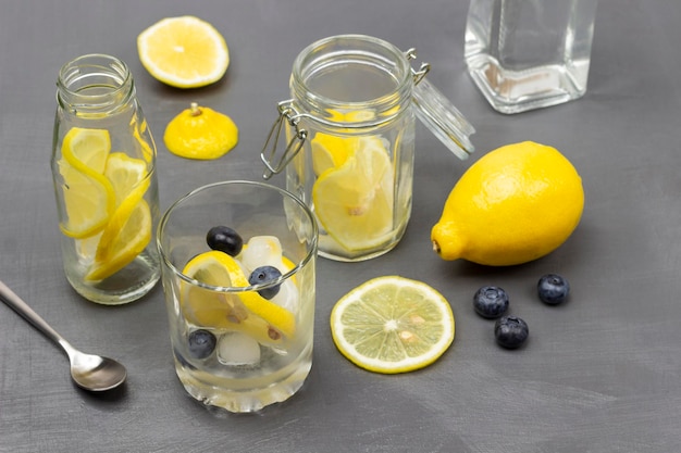 Sliced lemon in glass and in jar Bottled water Whole lemon and blueberries on table