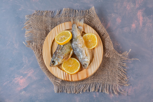 Sliced lemons and dried salted fish on a wooden plate on a burlap napkin, on the marble surface