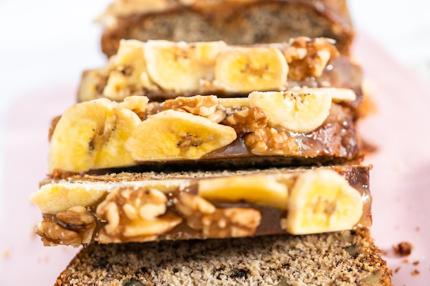 Sliced loaf of banana nut bread drizzled homemade caramel on a pink cutting board.