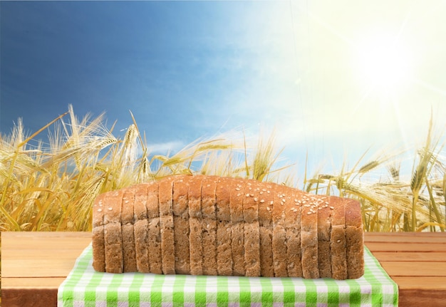 Sliced loaf of bread on wooden table with wheat field on background