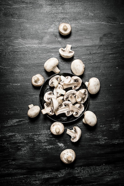 Sliced mushrooms in the pan. On black rustic table.