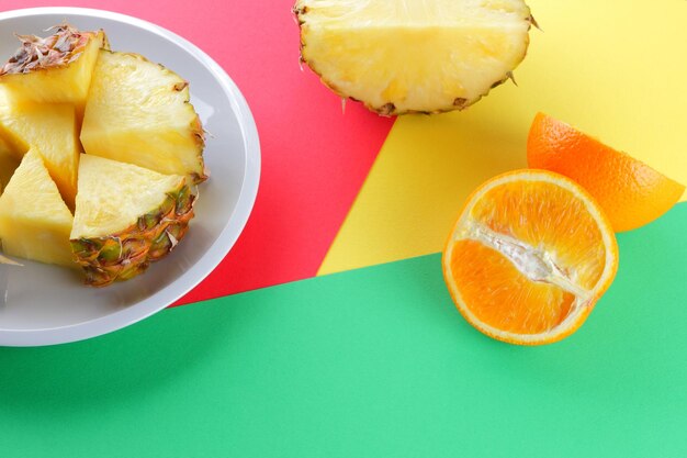 Sliced pineapple and oranges on multicolored background Pineapple and orange halves on white plate Close up