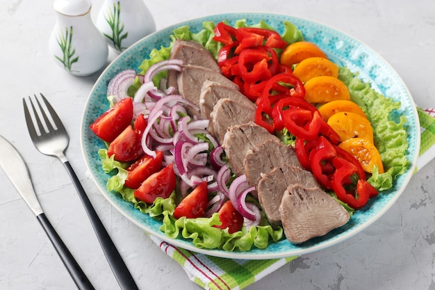 Photo sliced pork tongue with vegetables on blue plate on grey background. great cold appetizer. horizontal format. closeup