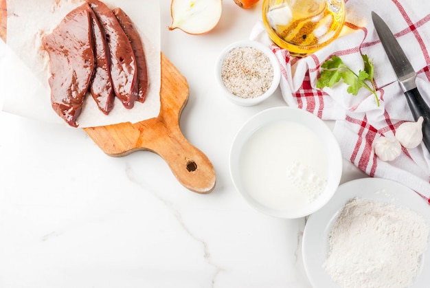 Sliced raw beef liver with spices, herbs, milk and flour, white marble table  top view