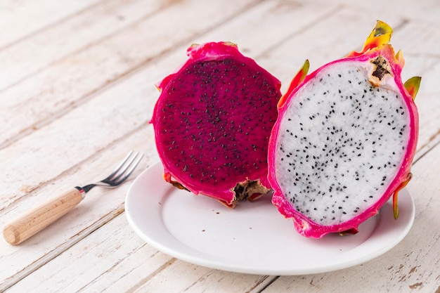 Sliced red dragon fruit, Costa Rican dragon fruit, purple pitaya, strawberry pear cactus and white dragon fruit in white ceramic plate on white old wood texture background with copy space, pitahaya